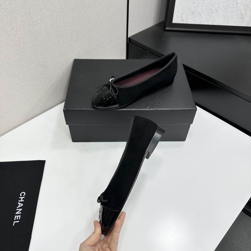 Black ballet flats with patent leather cap-toe and bow detail displayed on a black shoe box